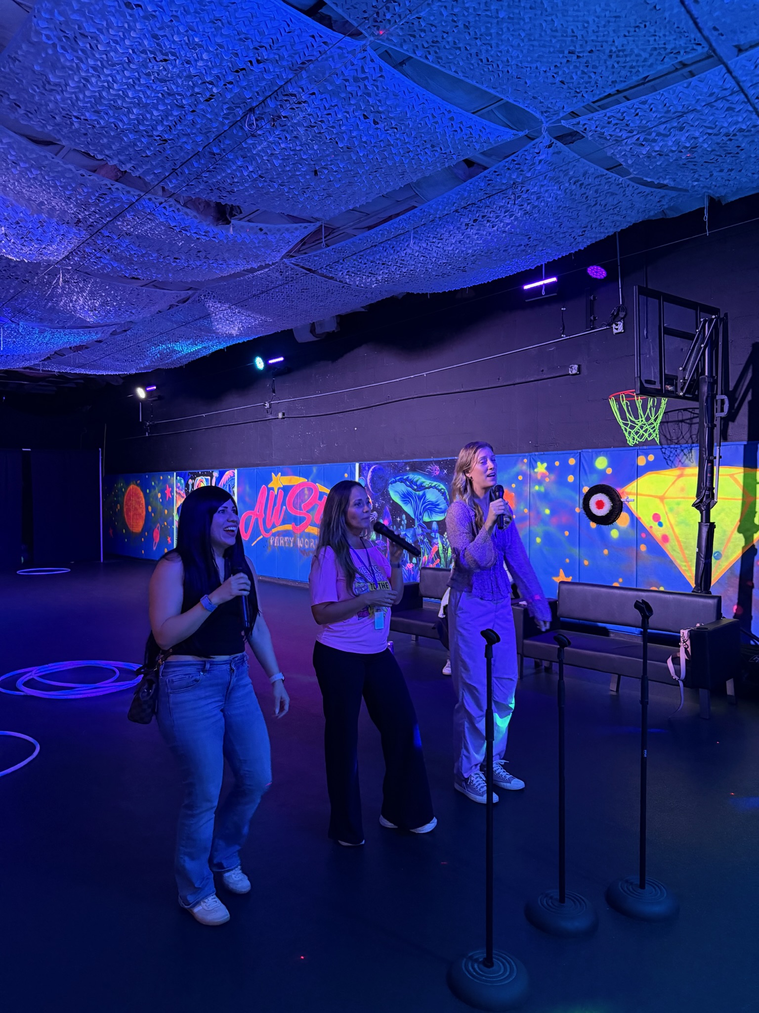 Group of young women singing on microphones in the All Star Party World karaoke lounge with stage lighting