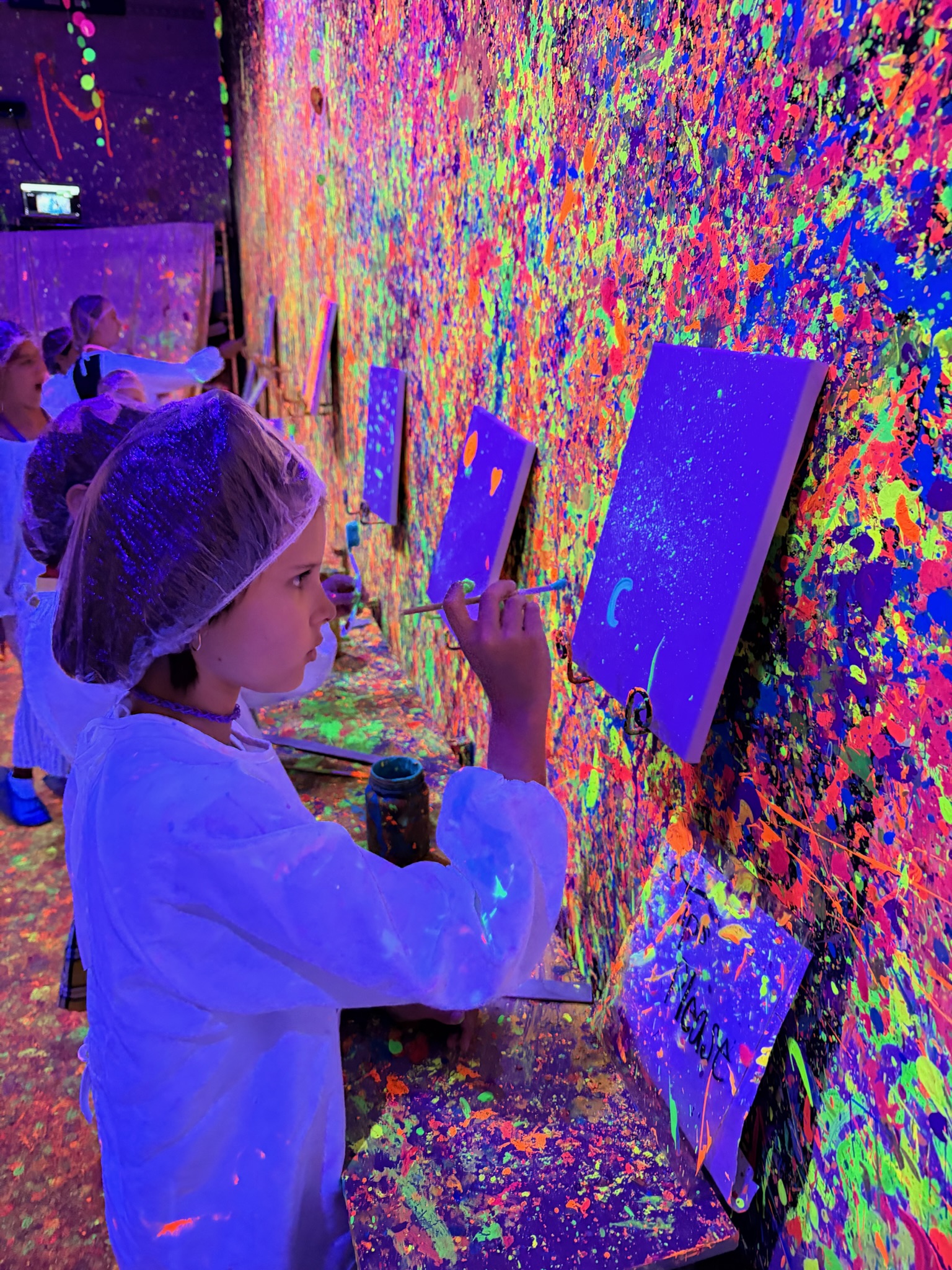 Close-up of a girl painting her canvas with neon paint under UV blacklights